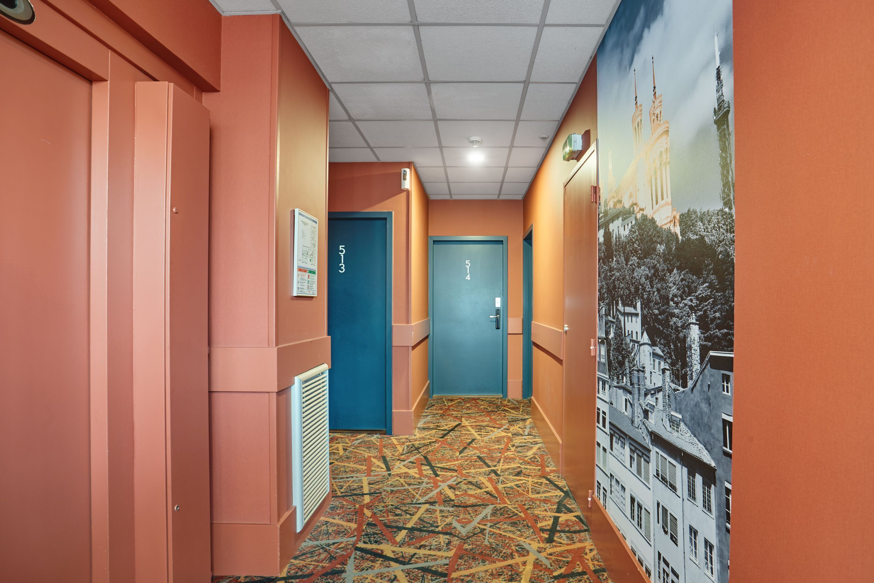 Un couloir aux murs orange, avec un tapis à motifs et des portes numérotées 513 et 514.