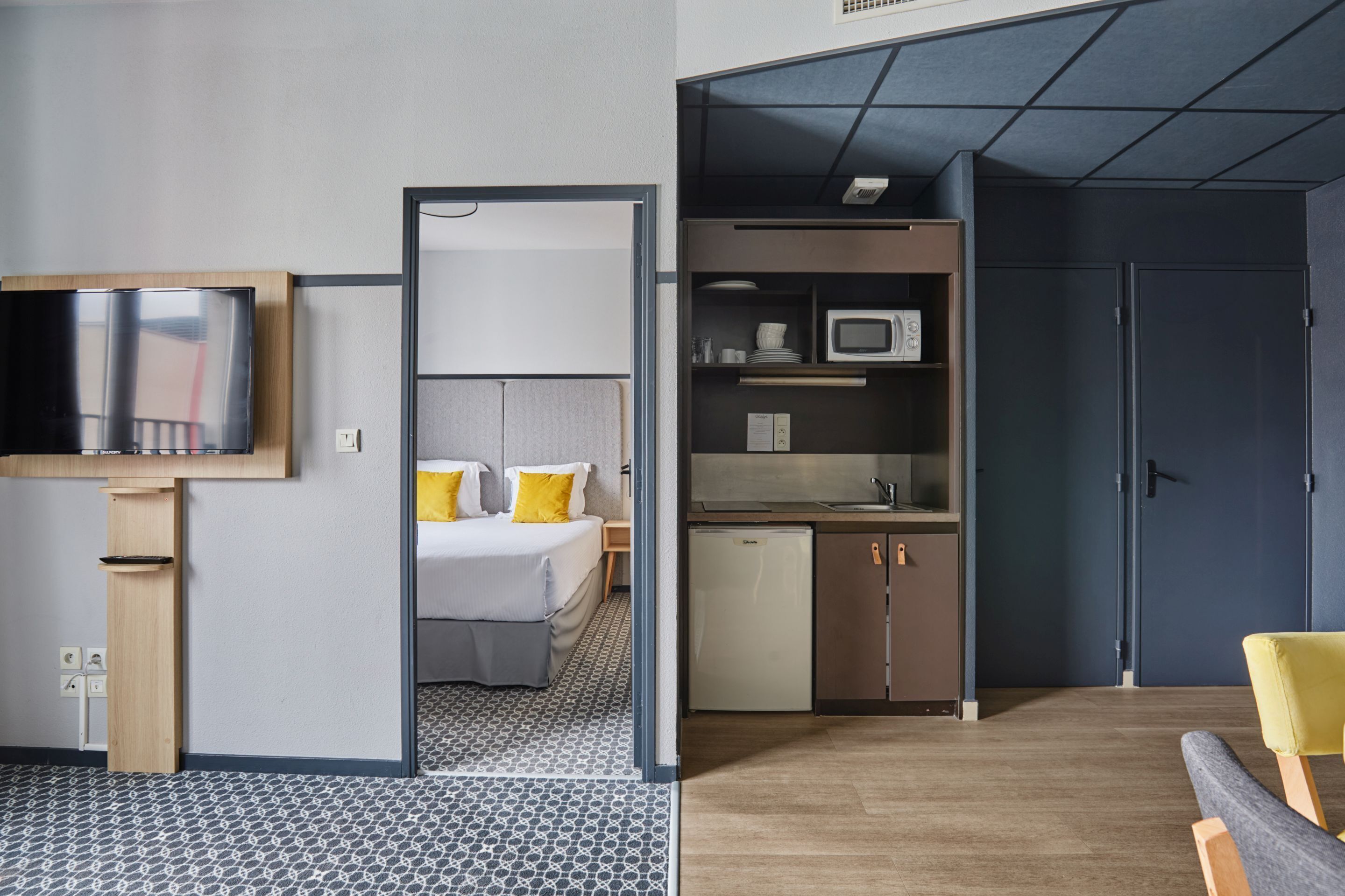 Une chambre d’hôtel équipée d’un lit, d’une télévision, d’une kitchenette et d’une porte donnant sur une autre pièce.