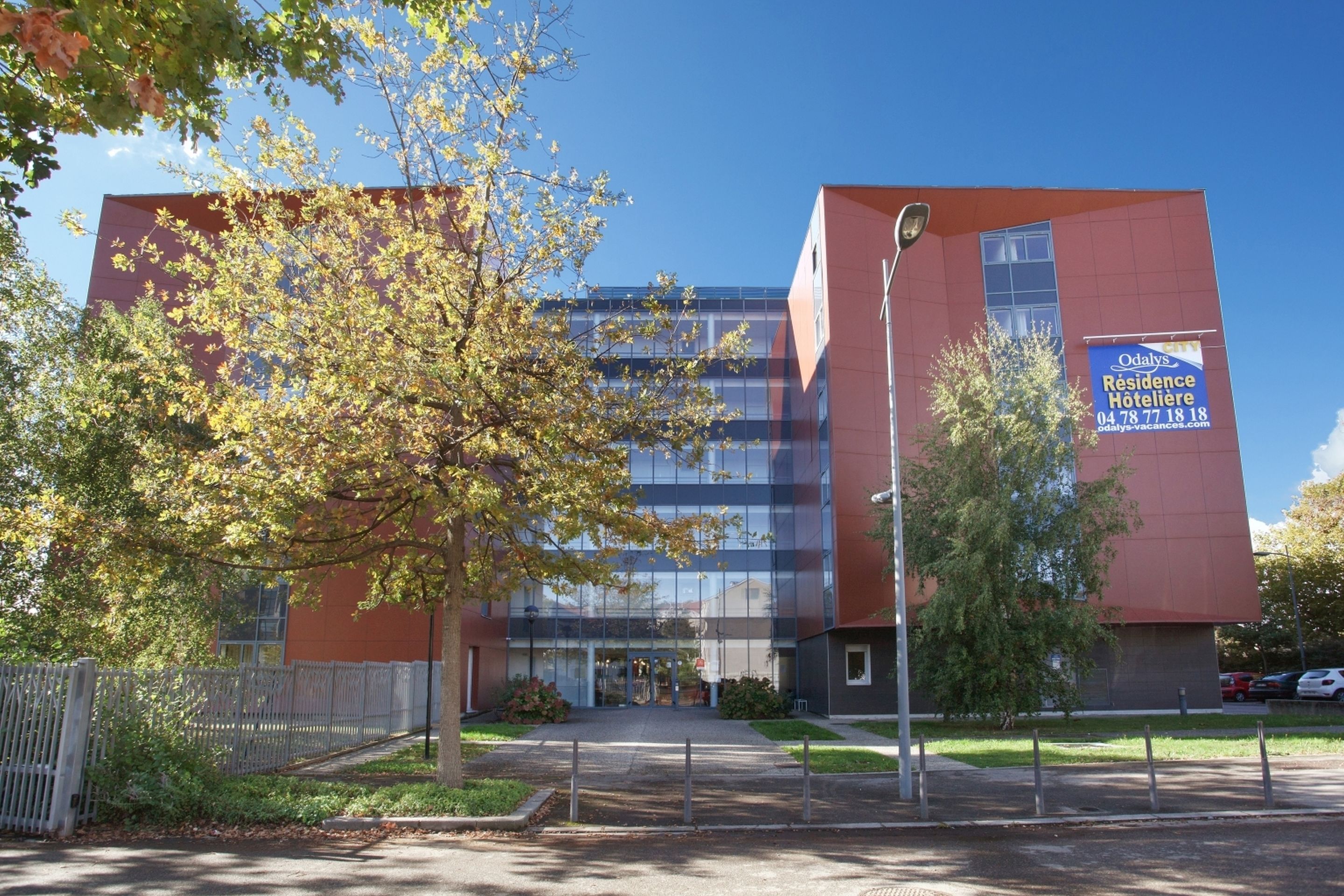 A modern building with a glass facade, a sign for Odalys Residence Hotelerie, and a clear sky.