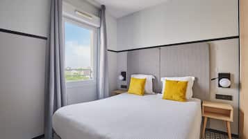 Ein Hotelzimmer mit einem großen Bett, zwei Nachttischen, einem Vorhangfenster und Blick auf die Stadt.