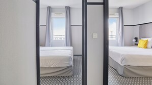 Habitación de hotel con dos camas, un ventanal con cortinas, suelo estampado y una lámpara de techo moderna.