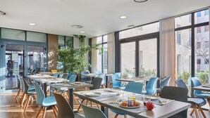 Un comedor moderno con mesas, sillas, ventanas amplias y plantas de interior.