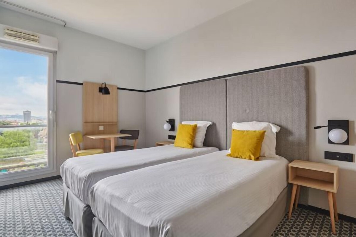 Habitación de hotel con dos camas, un escritorio, una silla y vistas a la ciudad.