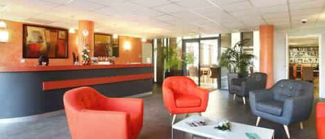 A modern reception area with a counter, red and grey armchairs, and a glass coffee table.
