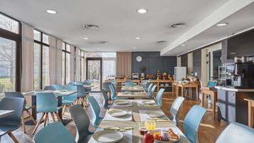 Un comedor moderno con mesas largas, sillas azules y una cocina al fondo.