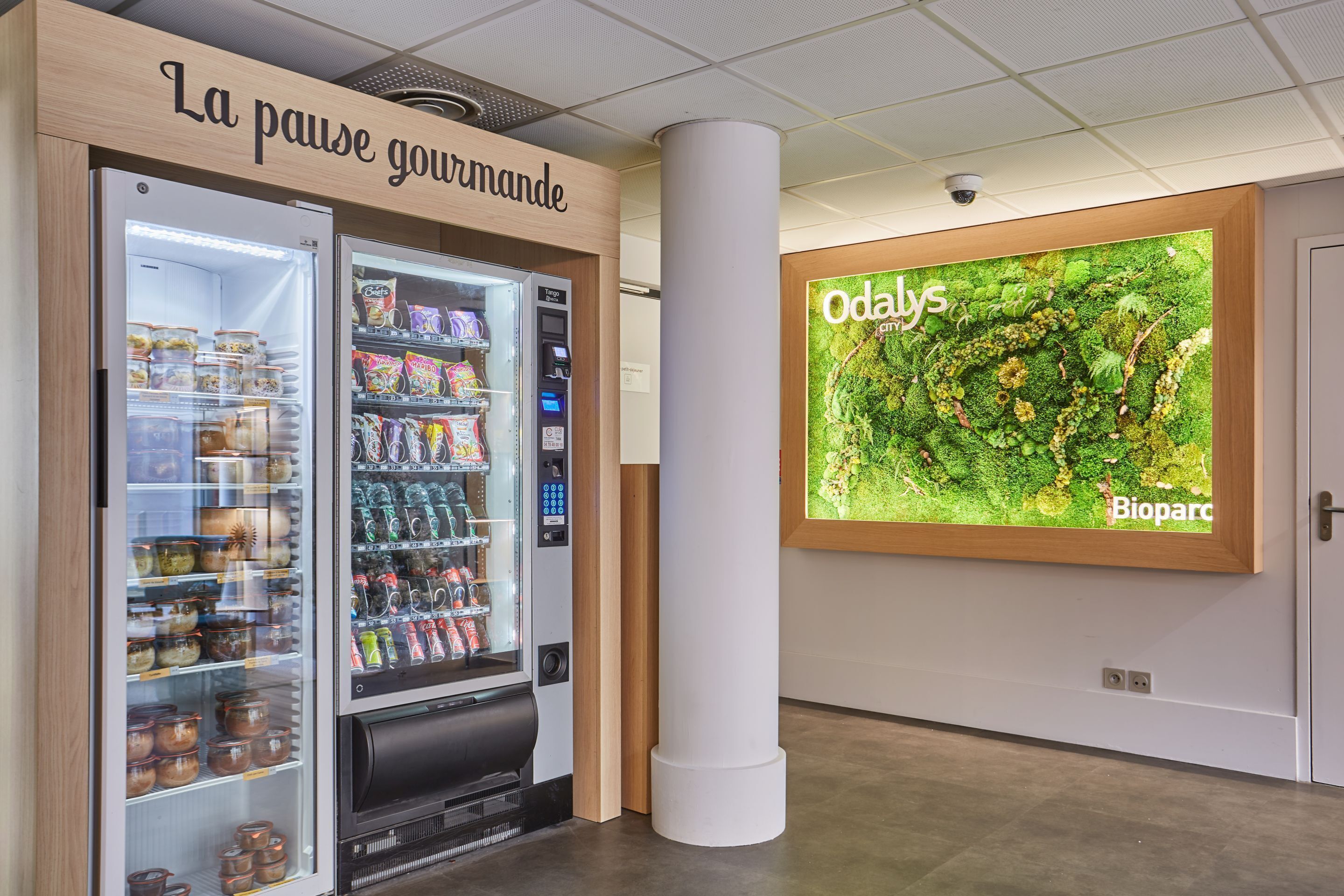 A vending machine with a variety of snacks and beverages, a sign reading "La pause gourmande," and a large wall display with the text "Odals" and "Bioparc."