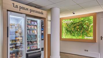 A vending machine with a variety of snacks and beverages, a sign reading "La pause gourmande," and a large wall display with the text "Odals" and "Bioparc."