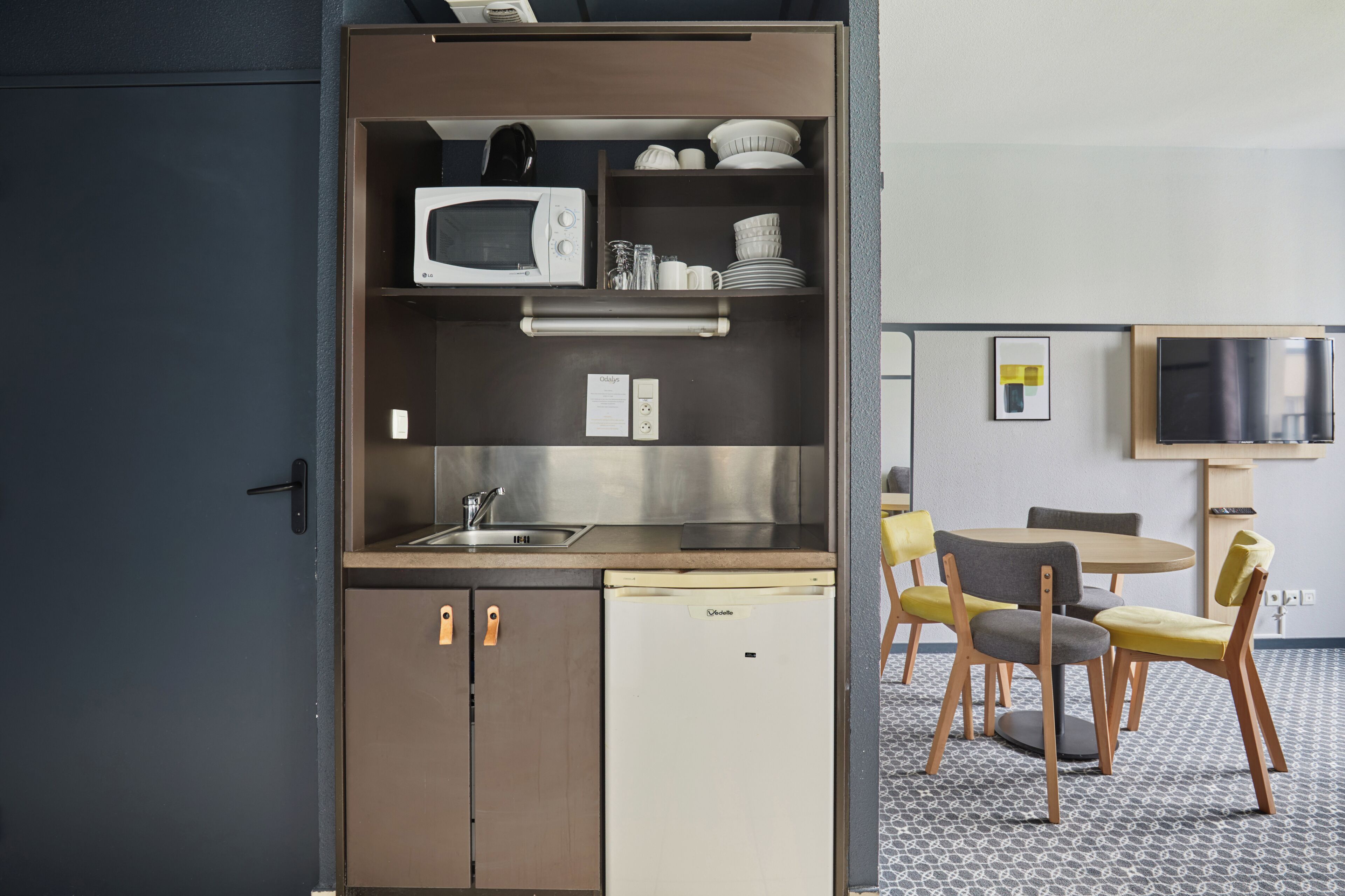 A compact kitchenette with a microwave, sink, and small refrigerator. There is a dining area with a table and chairs.