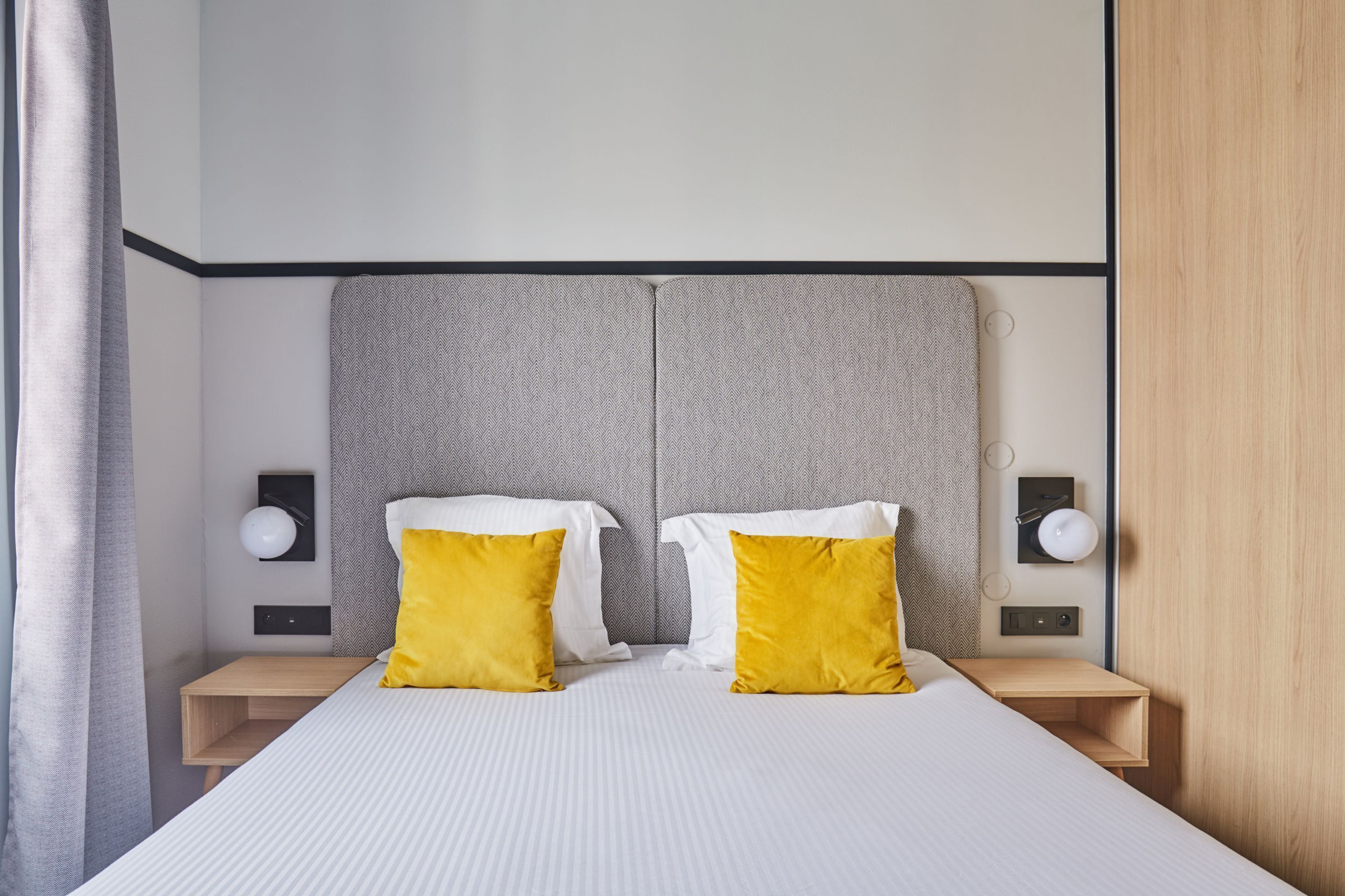 A modern hotel room with a large bed, two bedside tables, and a headboard.