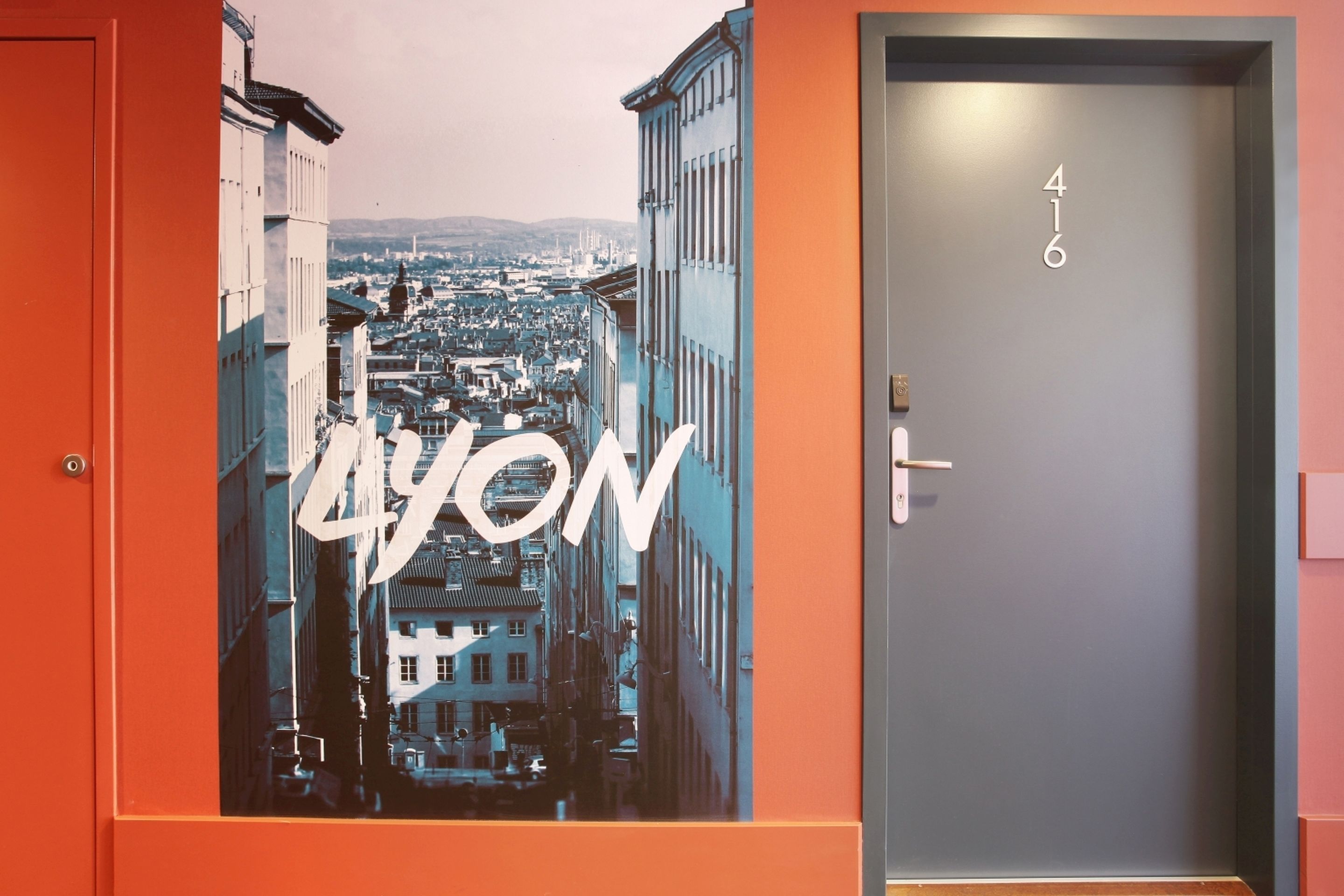 A hotel room with a large poster of a cityscape, a door with the number 416, and a red wall.
