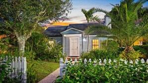 A house with a white door, surrounded by lush greenery and a white picket fence.