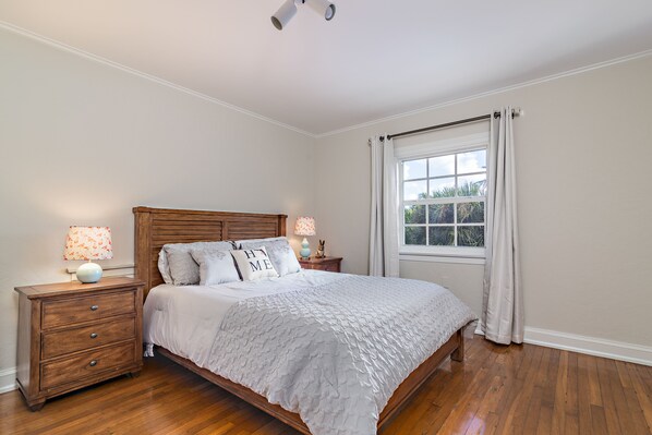 Un dormitorio con cama de madera, una mesita de noche con lámpara y una ventana con cortinas.