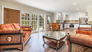 A spacious living room with a glass coffee table, two sofas with intricate designs, and a kitchen in the background.