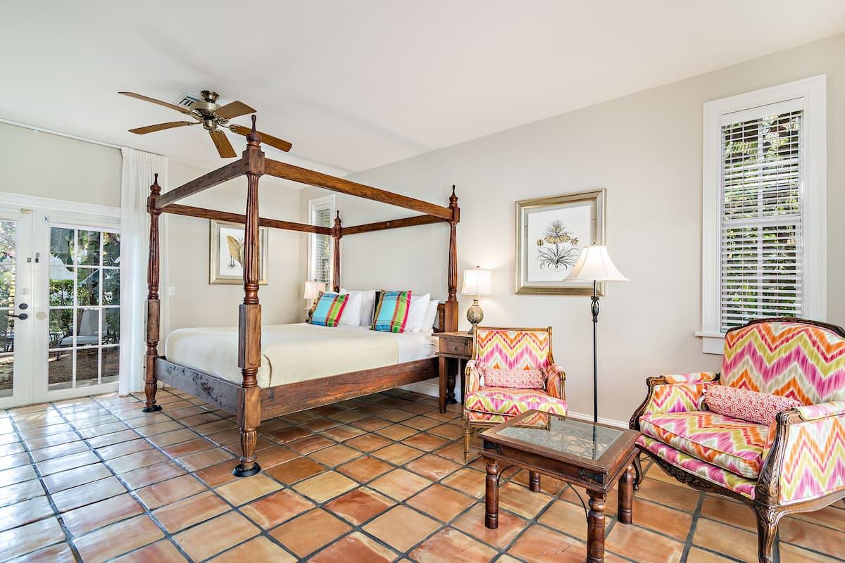 Un lit à baldaquin avec un ventilateur de plafond, une chaise à motifs en zigzag et une table avec un plateau en verre.