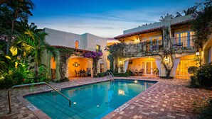 A swimming pool with a brick deck, surrounded by buildings with balconies and outdoor seating.