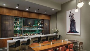 Eine moderne Bar mit einer langen Holztheke, mehreren Regalen voller Spirituosenflaschen und einem großen Flachbildfernseher. Es gibt mehrere Stühle und einen Esstisch mit Stühlen.