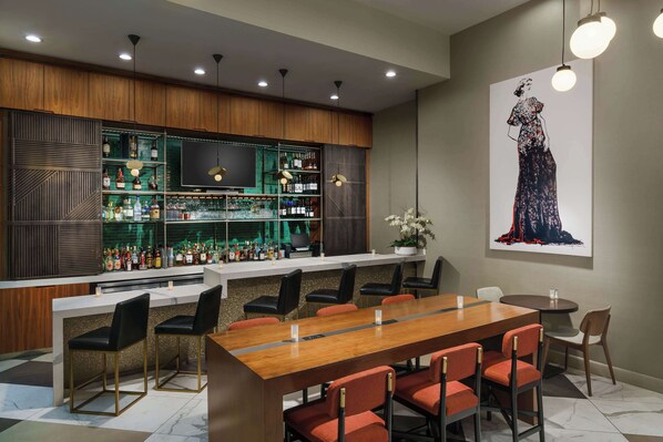 A modern bar area with a long wooden counter, multiple shelves of liquor bottles, and a large flat-screen TV. There are several chairs and a dining table with chairs. - DoubleTree by Hilton Hotel New York City - Chelsea (New York)