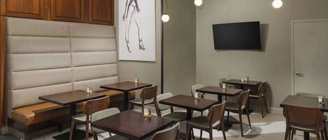 A restaurant with booth seating, tables, and chairs, a flat-screen TV mounted on the wall, and pendant lighting.