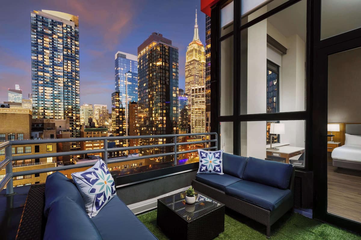 A balcony with a city view, furnished with a sofa, a coffee table, and decorative pillows.