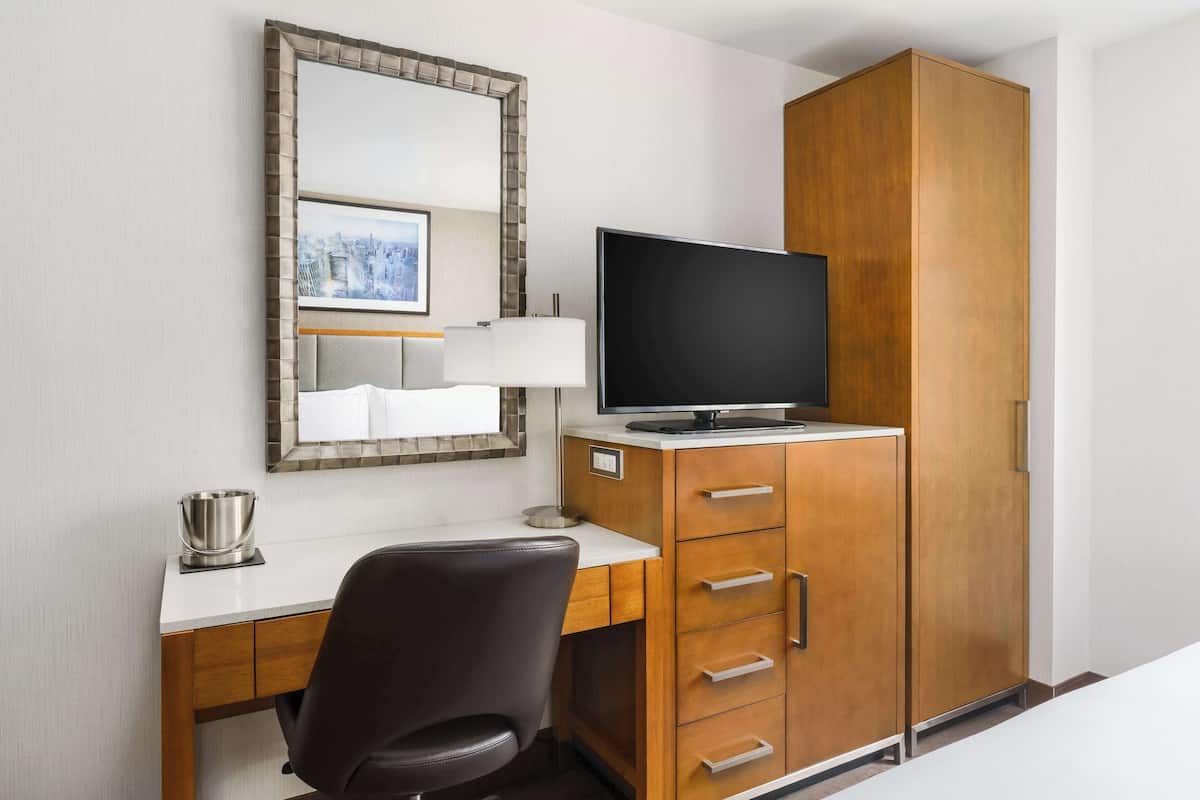 A hotel room with a wooden desk, a television, a mirror, and a wardrobe.