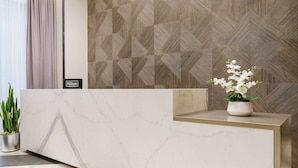 Ein Empfangsschalter mit Marmoroberfläche, eine geometrische Wand dahinter und eine Topforchidee auf der Theke.