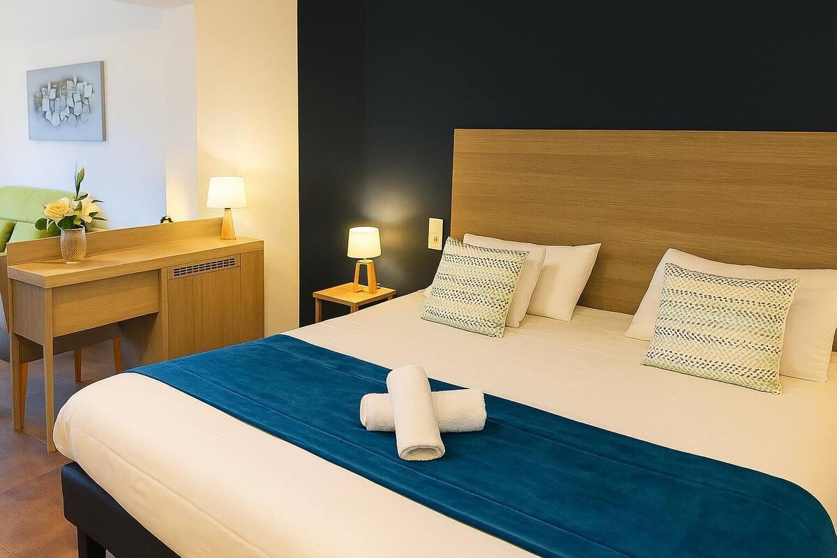 A hotel room with a bed, bedside tables, a desk, and a lamp.