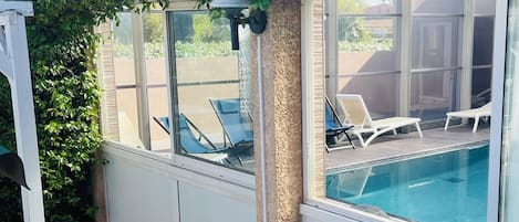 A poolside area with lounge chairs, a table, and a pergola covered with greenery.