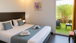A hotel room with a large bed, a headboard, a painting, and a view of an outdoor area with a table and chairs. - Hotel & Spa GIL DE FRANCE Cap D'Agde (Agde)