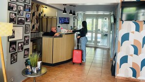 A reception area with a wooden counter, framed photos on the wall, a TV, and a potted plant. - Hotel & Spa GIL DE FRANCE Cap D'Agde (Agde)