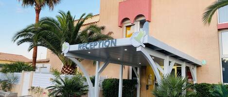 A reception area with a sign, palm trees, and potted plants.