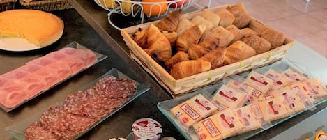 Uma mesa de buffet com diversos alimentos, incluindo frutas, doces, queijos e carnes.