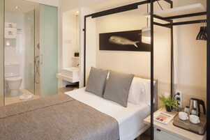 A modern bedroom with a four-poster bed, a sink, and a shower in the adjacent bathroom.