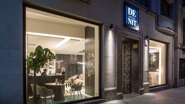 A modern hotel interior with a reception desk, seating area, and a large window. - Hotel Denit Barcelona (Barcelona)