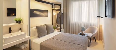 A modern hotel room with a large bed, a bedside table, a mirror, a dresser, and a window with curtains.