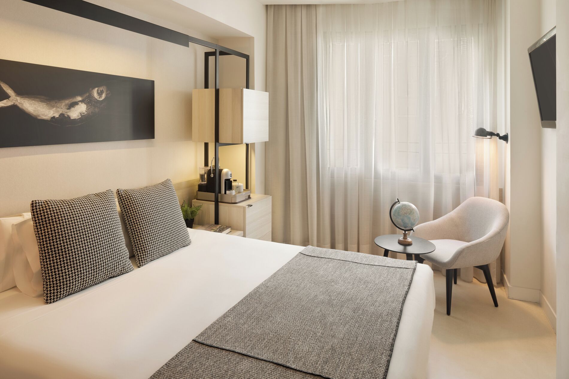 Ein Hotelzimmer mit einem großen Bett, zwei gemusterten Kissen, einem Nachttisch mit Lampe, einem Globus und einem Sessel.