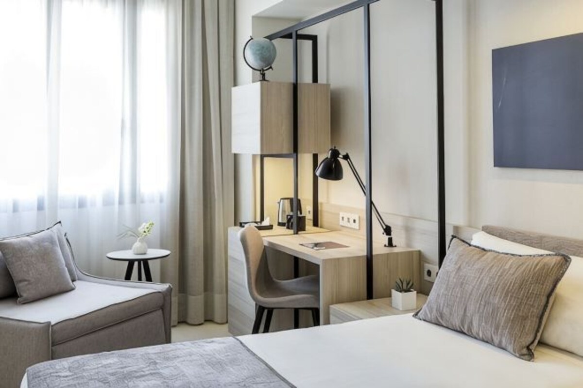 Habitación de hotel con una cama, un escritorio, una silla, una mesita y una lámpara.