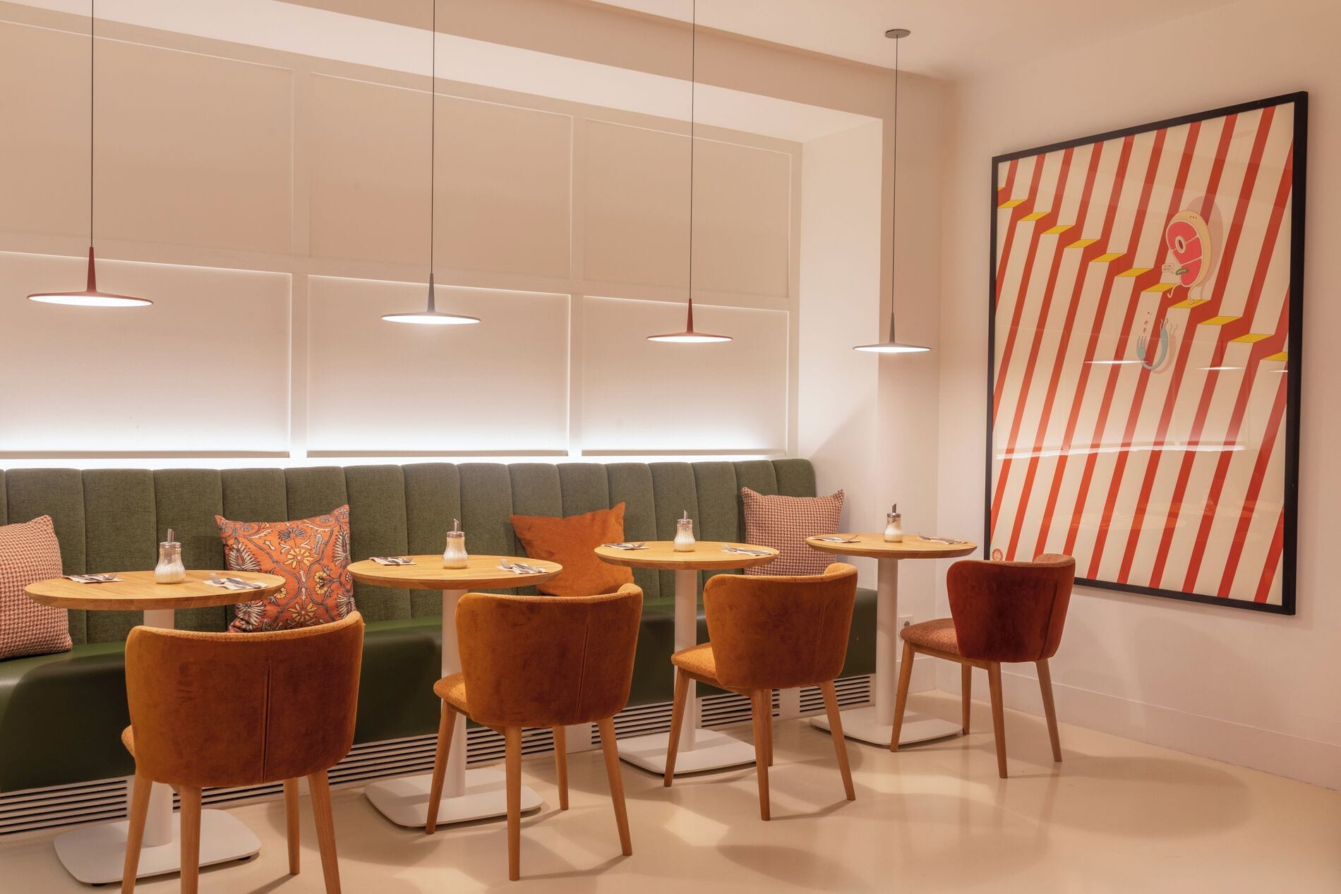 Un interior moderno con un sofá verde, mesas redondas y sillas naranjas.