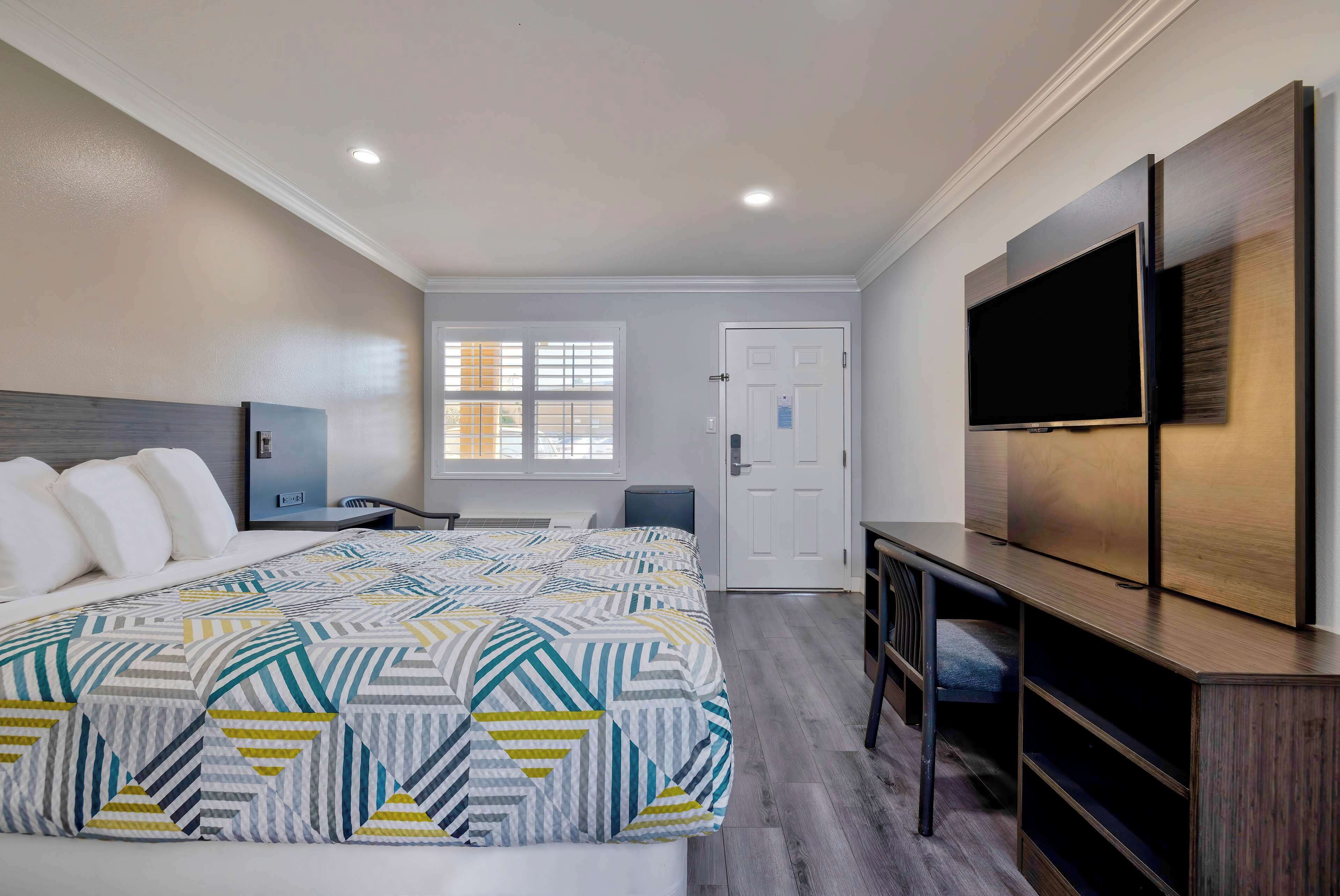 A hotel room with a bed, a TV, a desk, and a window.