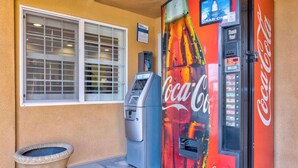 A Coca-Cola branded vending machine next to a window with blinds, a small planter, and a sign above the window. - Motel 6 South Gate, CA (South Gate)