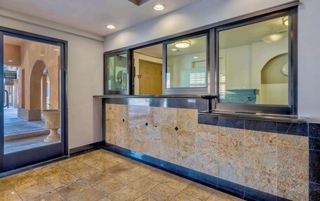 A lobby with a marble floor, a reception desk, and a glass door leading to an outdoor area.