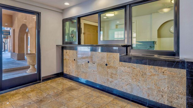 A lobby with a marble floor, a reception desk, and a glass door leading to an outdoor area. - Motel 6 South Gate, CA (South Gate)