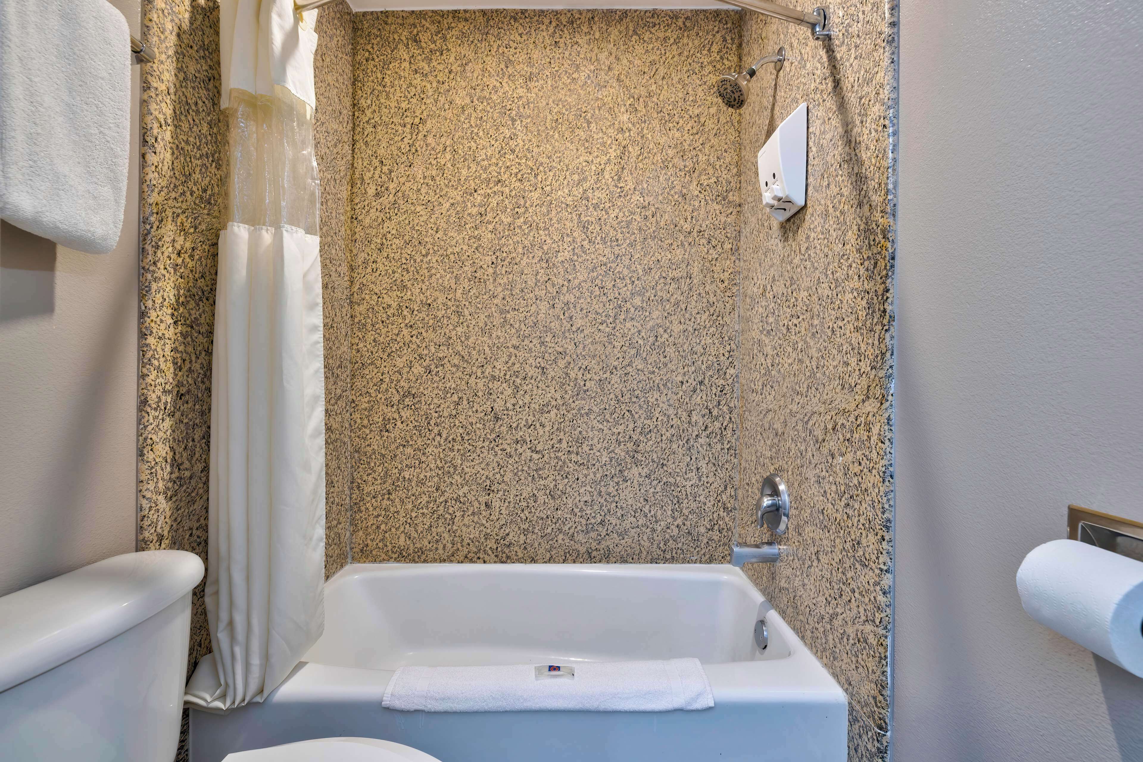 A bathroom with a bathtub, a toilet, a shower curtain, and a towel rack.