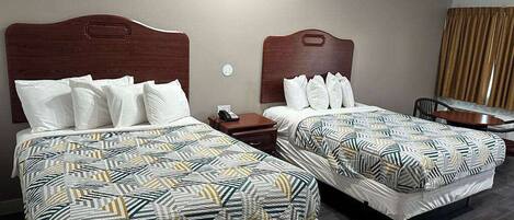 Quarto de hotel com duas camas, cada uma com roupa de cama estampada e cabeceiras de madeira.