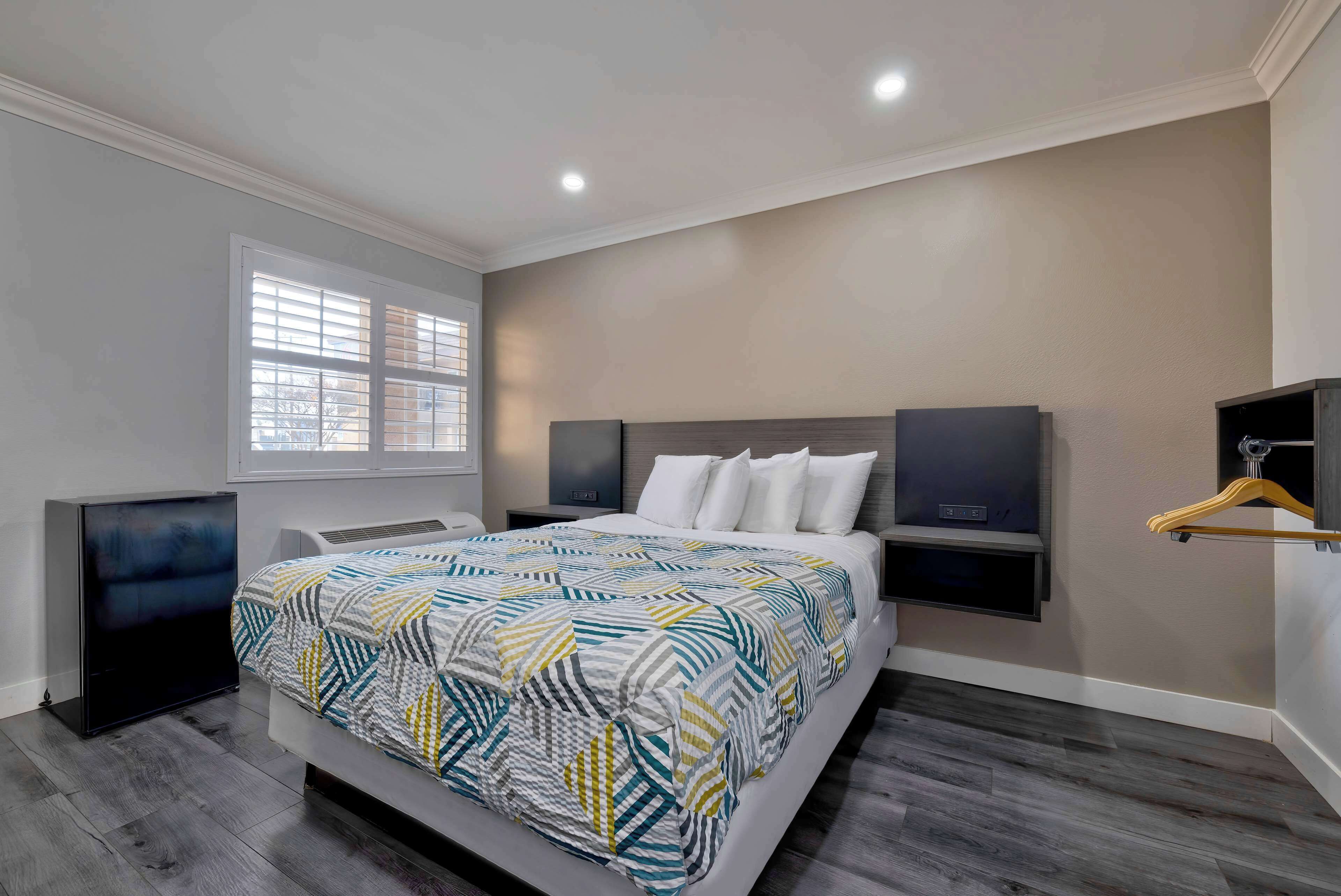 A modern bedroom with a large bed, built-in TV, and a window with blinds.