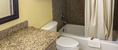 Un baño con encimera de granito, inodoro, bañera y cortina de ducha.