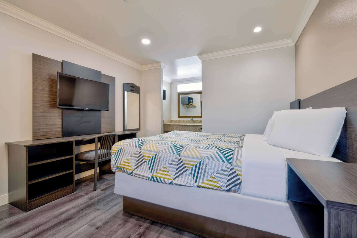 A hotel room with a bed, a desk, a TV, and a mirror.