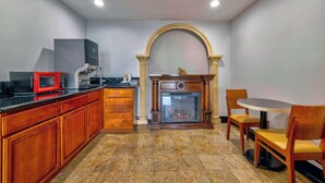 A kitchen with a built-in microwave, wooden cabinets, a fireplace, and a dining area with a round table and chairs. - Motel 6 South Gate, CA (South Gate)