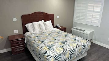 Un dormitorio con cama, mesita de noche, cómoda, ventana con persianas y un equipo de aire acondicionado.
