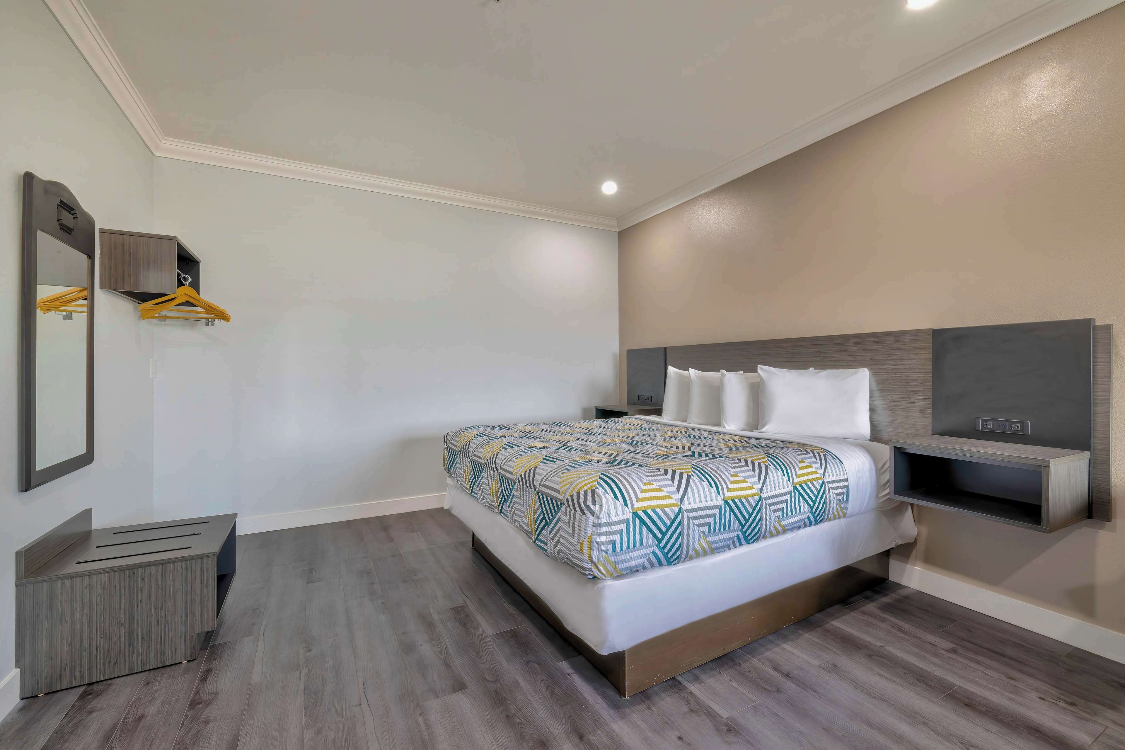 A modern hotel room with a large bed, a bedside table, a mirror, and a wardrobe with a hanging rack.