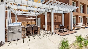 An outdoor patio with a grill, seating area, and a pergola.